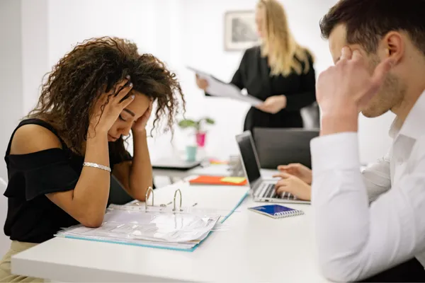 two people with head in hadns while another presents at a white board