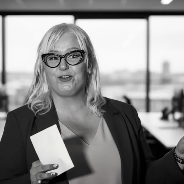 Jennifer Goldie presenting with blonde medium lenght hair and black cats eye hape glasses holding a prompt card in left hand