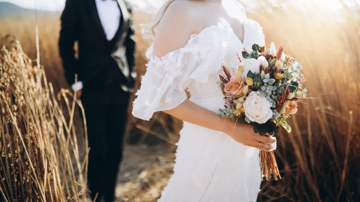 Bride holding a bouquet with groom in the background, representing marriage as a life event that may prompt an insurance review