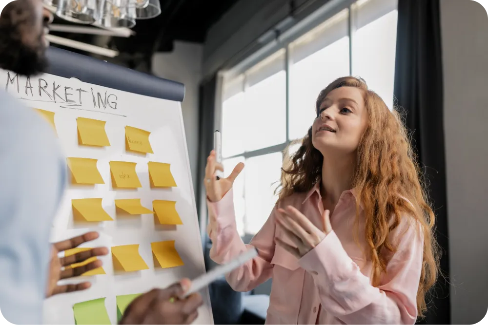 an image of a woman talking with a man about the marketing strategies on the whiteboard behind them