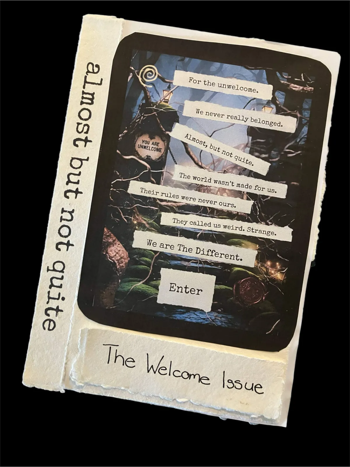 A collage of hand-made zine elements and art materials arranged on a black background. Torn strips of cream parchment display typed phrases such as “We are The Different” and “The world wasn’t made for us.” A metal ruler and gold pen lie across the page. A small metal dish holds melted sealing wax with a wax seal stamp resting inside. A hand is carefully positioning a strip of words onto a printed image. Nearby are wax seals in burgundy, gold, and bronze, and scraps of text, tape, and paper.