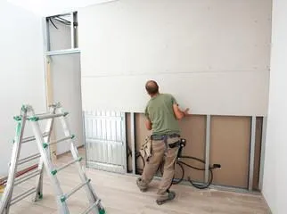 Man hanging drywall seet on wall