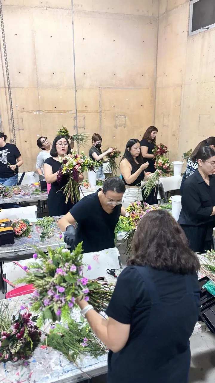 Retrato editorial de instructora mostrando composición floral media luna, fondo crema, énfasis en manos y técnica profesional.