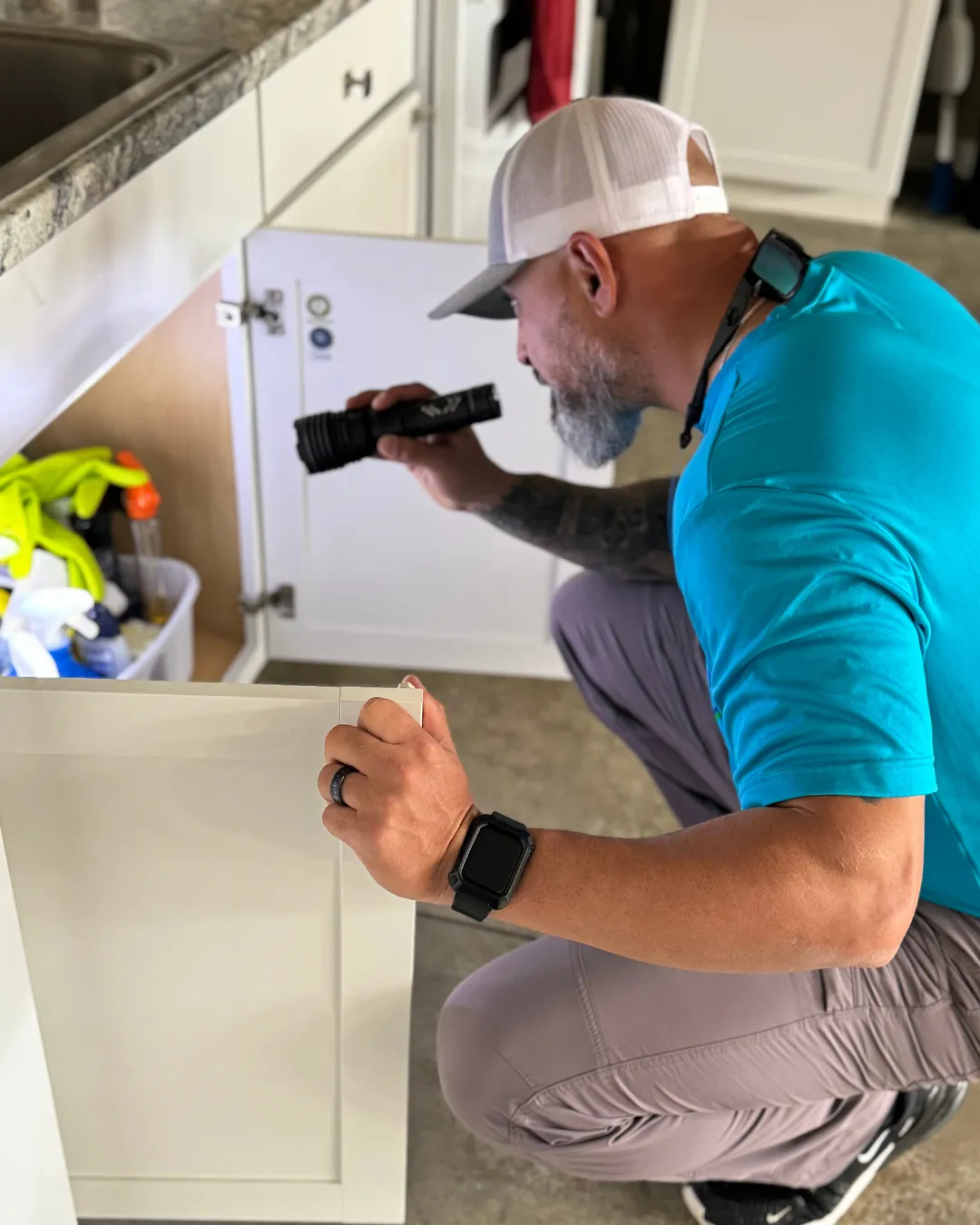 shield pest technician checking for rodent activity underneath a sink