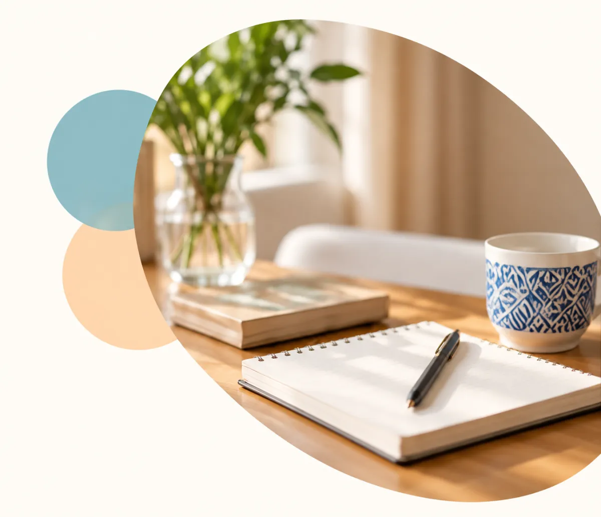 Notebook, pen, and a cup on a wooden desk with a plant in the background.