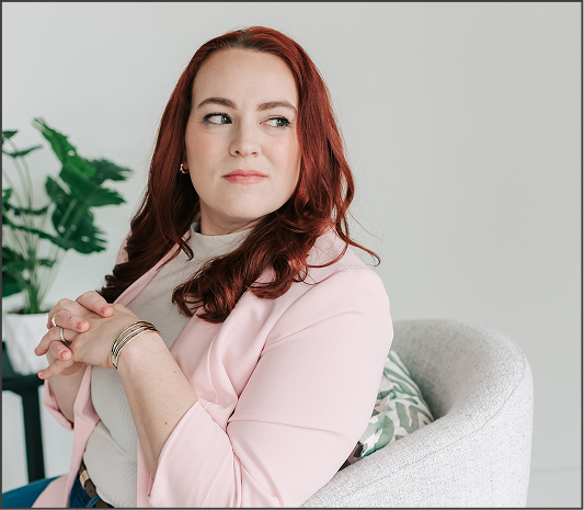 Portrait of Berkeley County VW bookkeeper Jamie, a woman with wavy red hair in pink blazer, looking back thoughtfully.