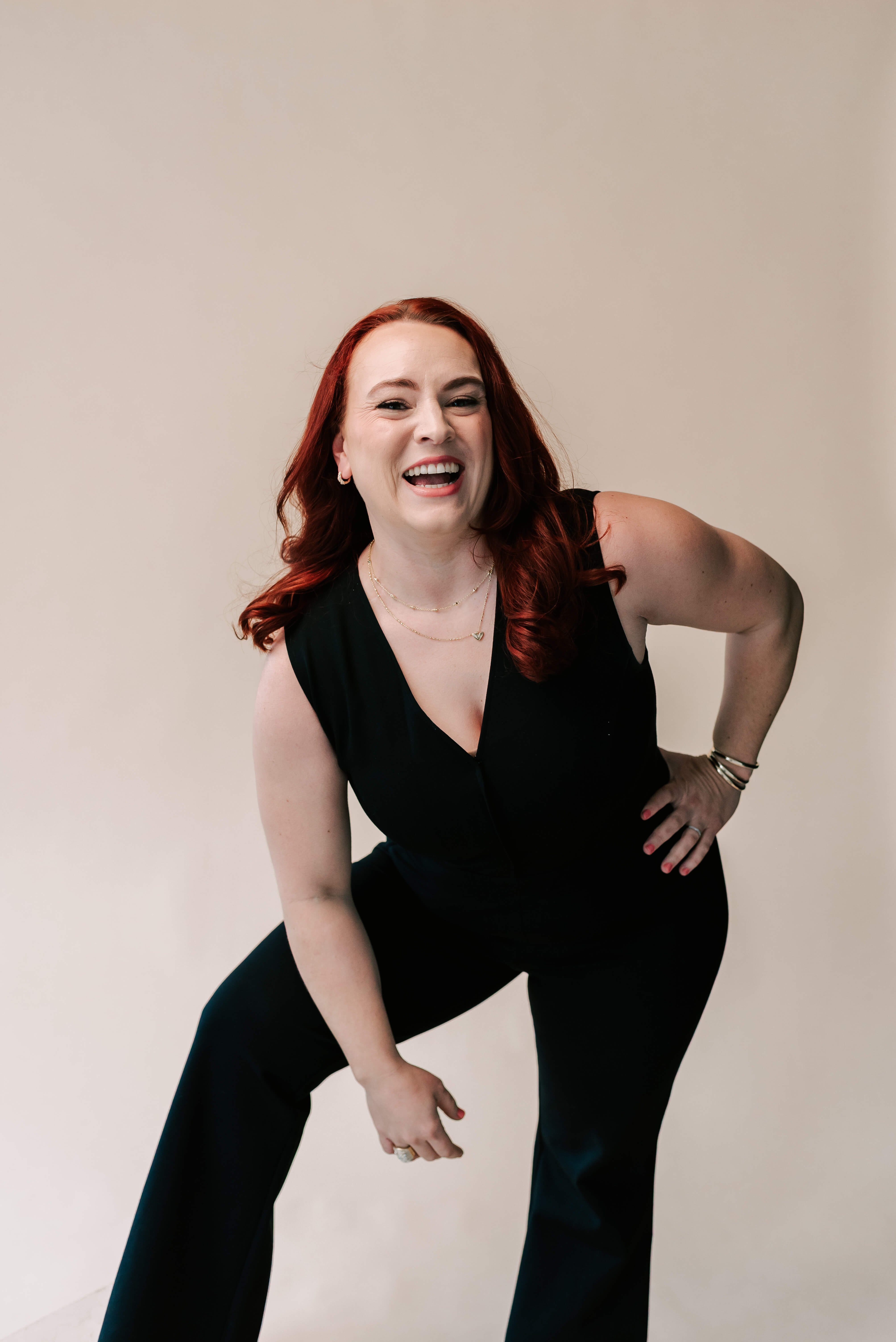 Smiling red-haired Berkeley County VW bookkeeper Jamie leans forward in a black sleeveless jumpsuit with gold jewelry.