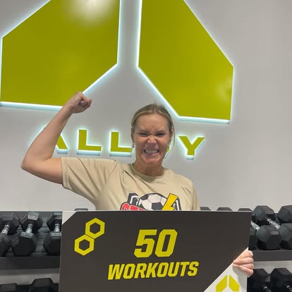 Two Alloy Personal Training Kaysville members holding milestone signs for their first and fiftieth workouts in a small group personal training studio for adults over 40.
