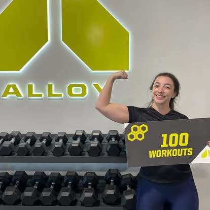 Alloy Personal Training Kaysville members holding 25 and 150 workout milestone signs in a small group personal training studio designed for adults over 40.