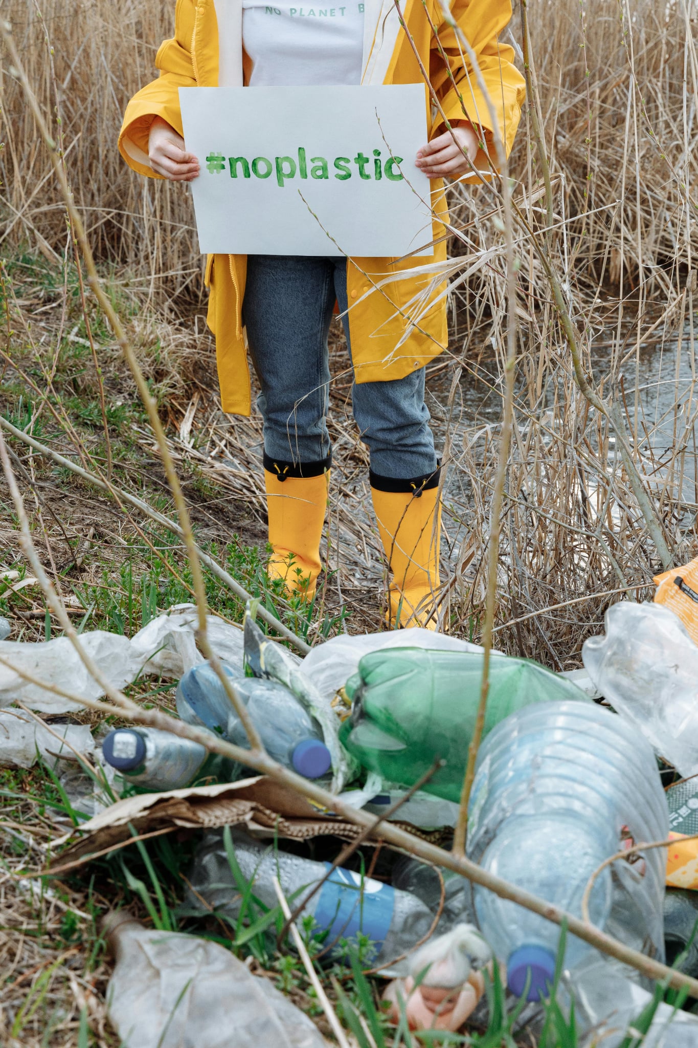 lady in white trench coat holding a #noplastic sign up behind junk