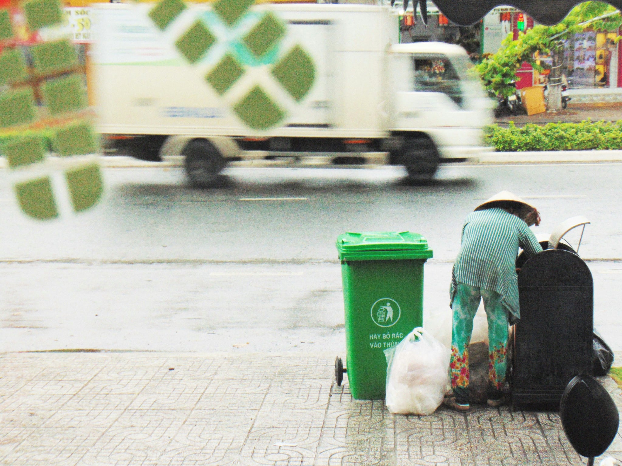 lady taking trash out from street bins with truck driving pass her on road