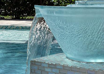 Close-up of a glass water bowl feature with cascading flow into a luxury swimming pool, accented by mosaic tile.