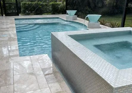 Luxury pool with raised spa covered in mosaic tile, featuring dual water bowl fountains and surrounded by light stone decking.
