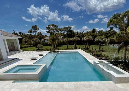 Spacious backyard with modern rectangular pool and attached spa, surrounded by stone deck and tropical landscaping.