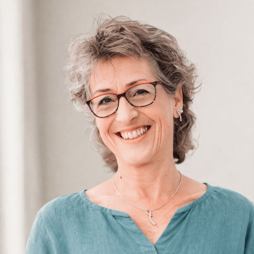 Claudia Hausheer in petrolfarbener Bluse lächelt herzlich vor heller Wand