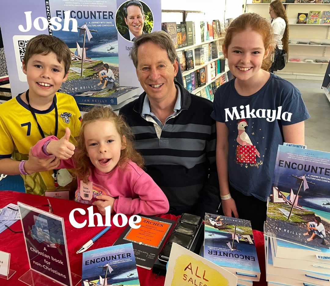 Author Ian Reilly signing copies of Encounter at a bookshop event, smiling with children at a table displaying his Christian memoir about Samoa and culture shock.