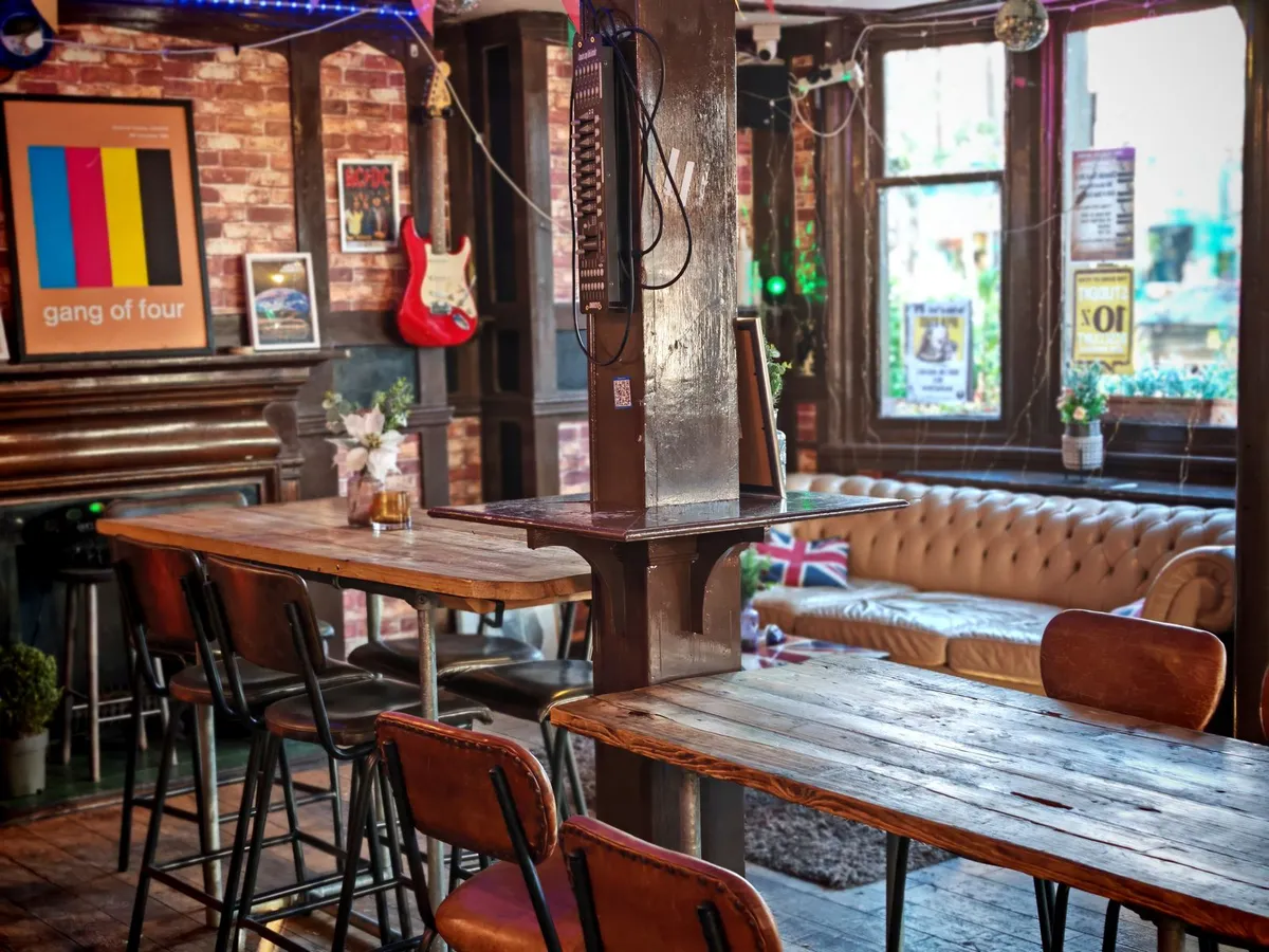 A bright, warm English pub interior with rustic wooden tables, leather seating and daylight through the windows
