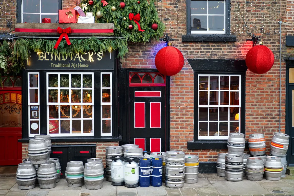 A bright, festive British pub front decorated for Christmas with greenery, red baubles and stacked beer kegs
