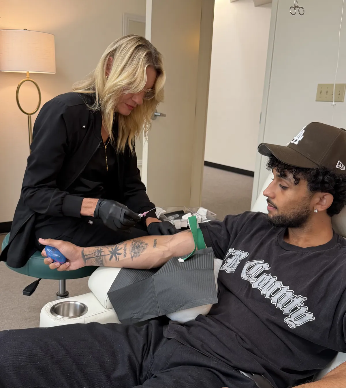 A nurse attending to the arm of a seated person wearing a cap