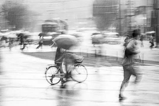 A man pushing his bicycle and another sprinting across a Kumamoto street in torrential rain, a layered crowd crossing behind them in opposing directions, monochrome ICM fine art photograph by Angie Harker