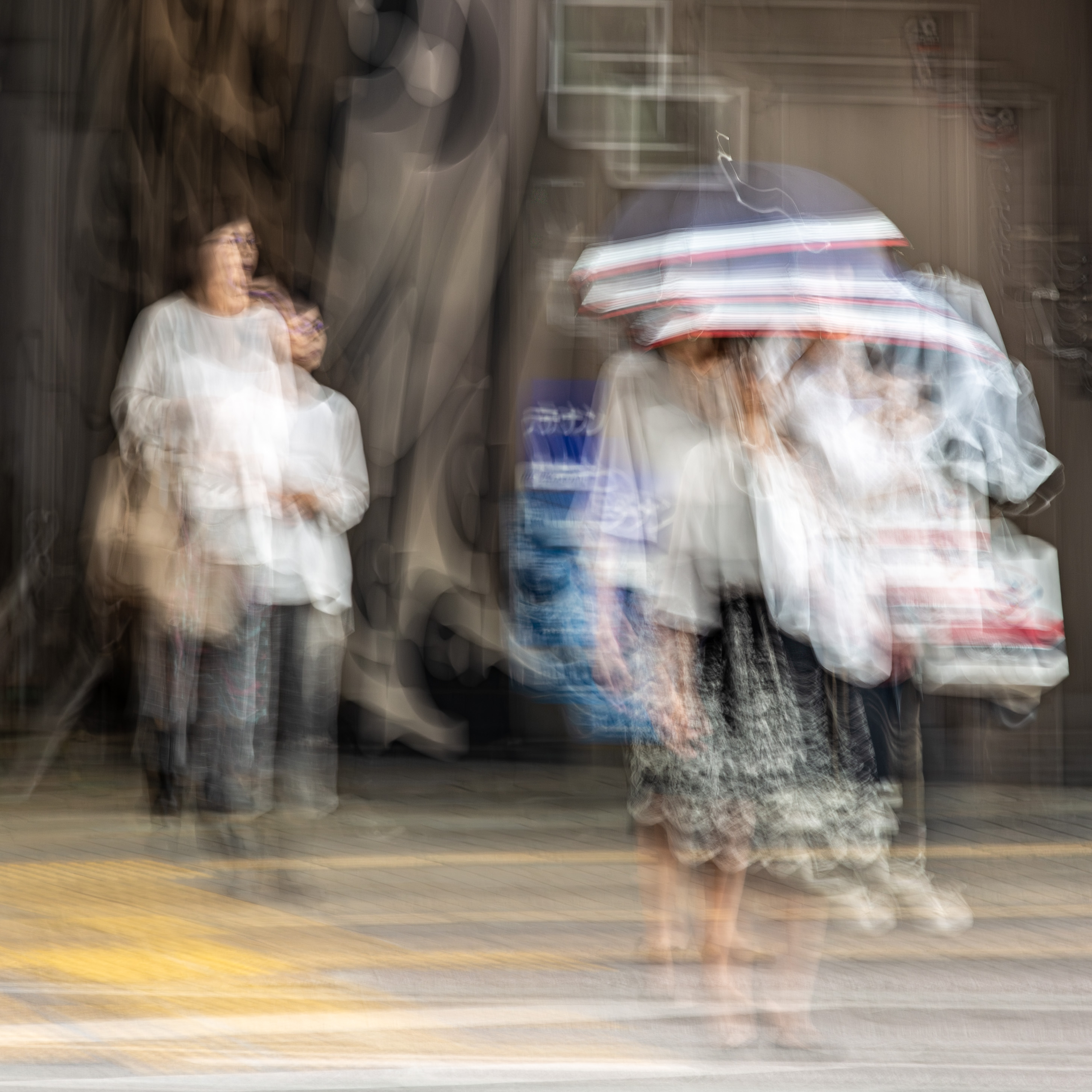 Long exposure ICM photograph of figures in tropical rain on a Kumamoto street, two emotional states caught simultaneously in a single frame, by fine art photographer Angie Harker