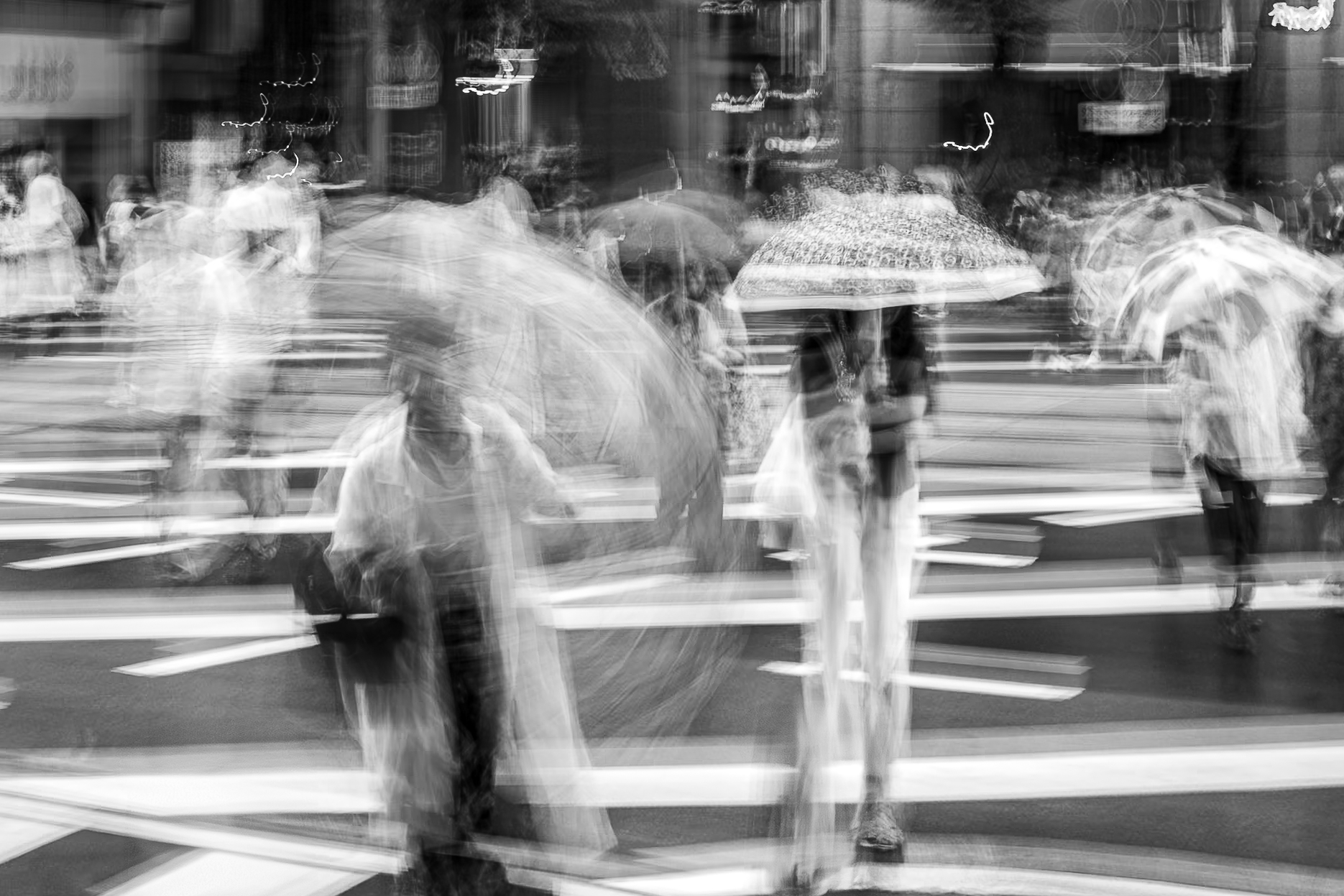 Umbrellas spinning and figures seeking cover as pedestrians cross toward the camera through torrential rain in Kumamoto, Japan, monochrome ICM fine art photograph by Angie Harker