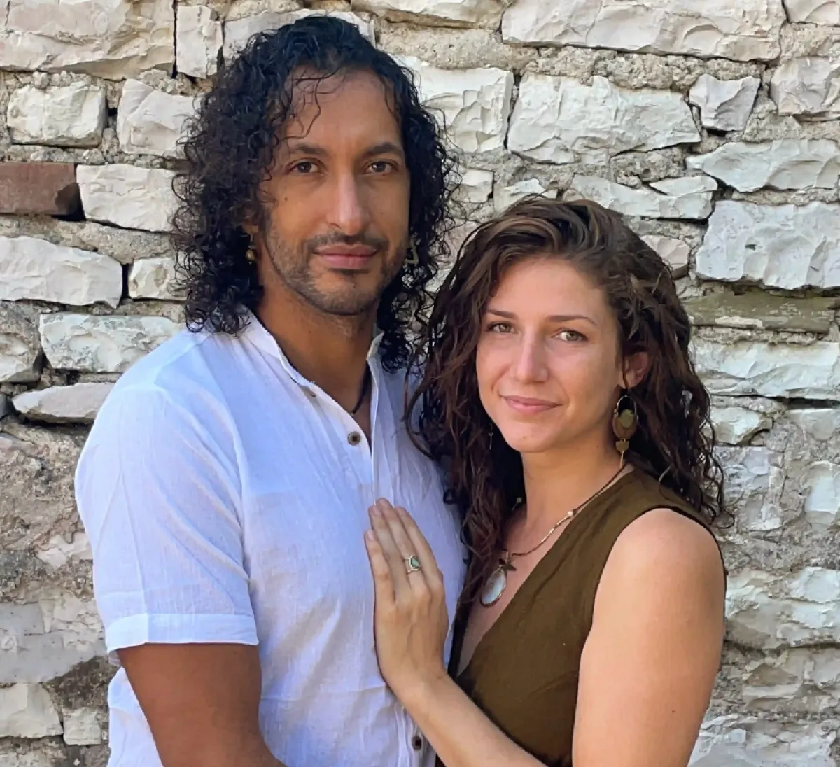 A portrait of the webinar host, a smiling middle-aged woman of South Asian descent, wearing flowing earth-toned clothing, seated cross-legged in a sunlit studio with plants and books in the background.