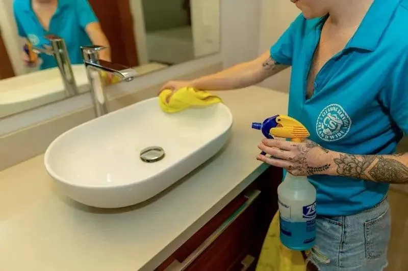 Housekeeper cleaning a bathroom sink with gloves and sponge