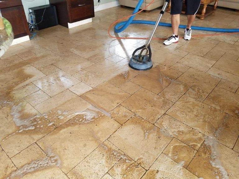 CSI worker using a floor cleaning machine on dirty tile flooring.