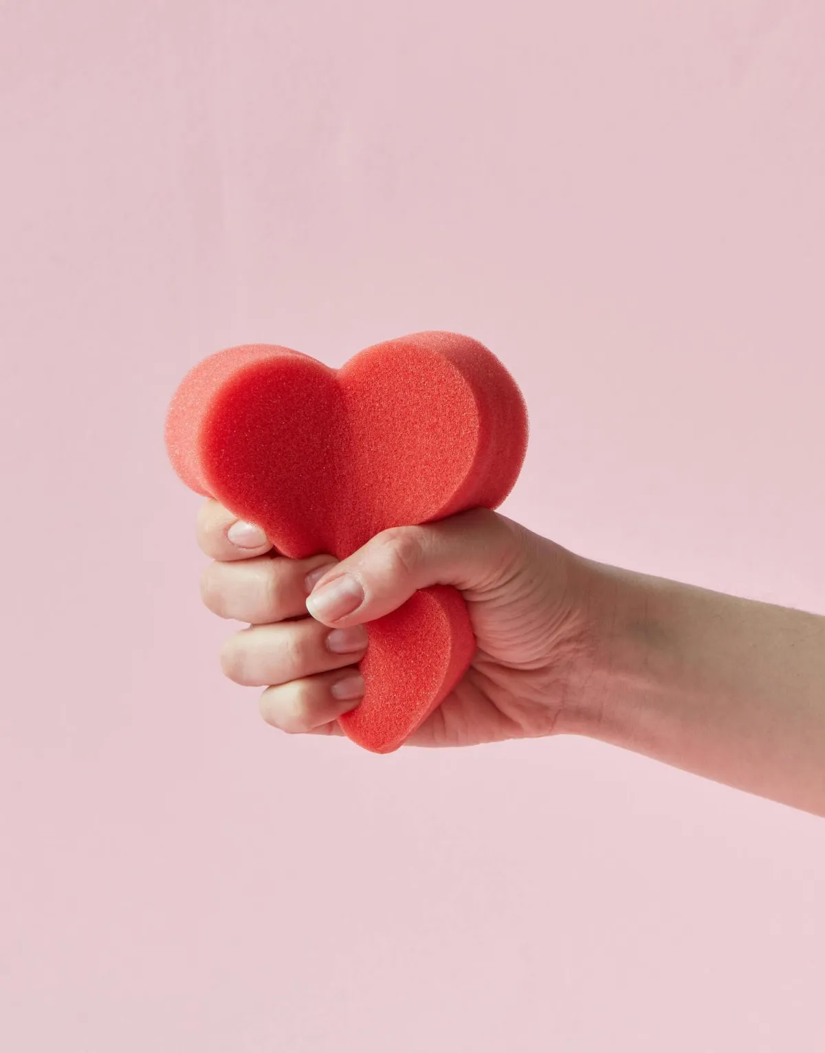 light skinned hand squeezing a red sponge heart