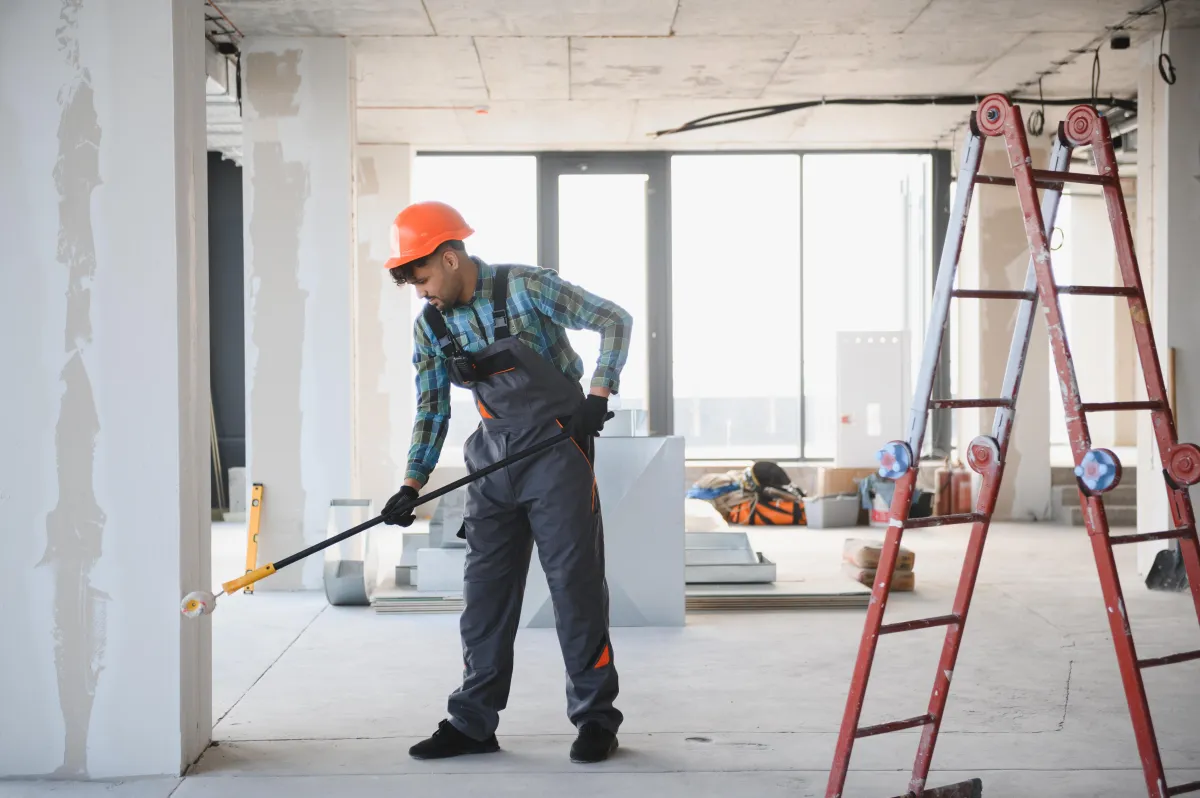 Construction worker painting walls with roller brush on telescopic handle
