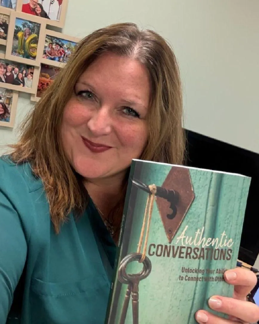Abigail Doust, Christian certified coach and author, smiling while holding her faith-based communication guide Authentic Conversations.