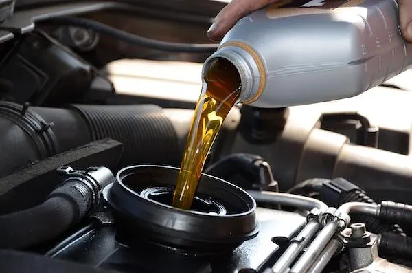 Close-up of technician pouring conventional motor oil into a car engine at United Oil Change Club in Garden City, providing quick and affordable oil change service.