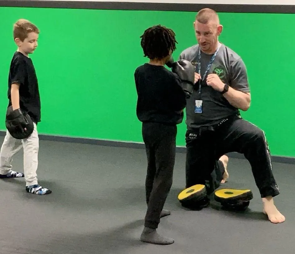 Instructor kneeling to greet a young child at eye level in a friendly, welcoming way.