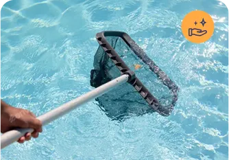 Person using a pool skimmer to clean debris from a sparkling blue swimming pool, illustrating Strong Tower Pool's maintenance services.