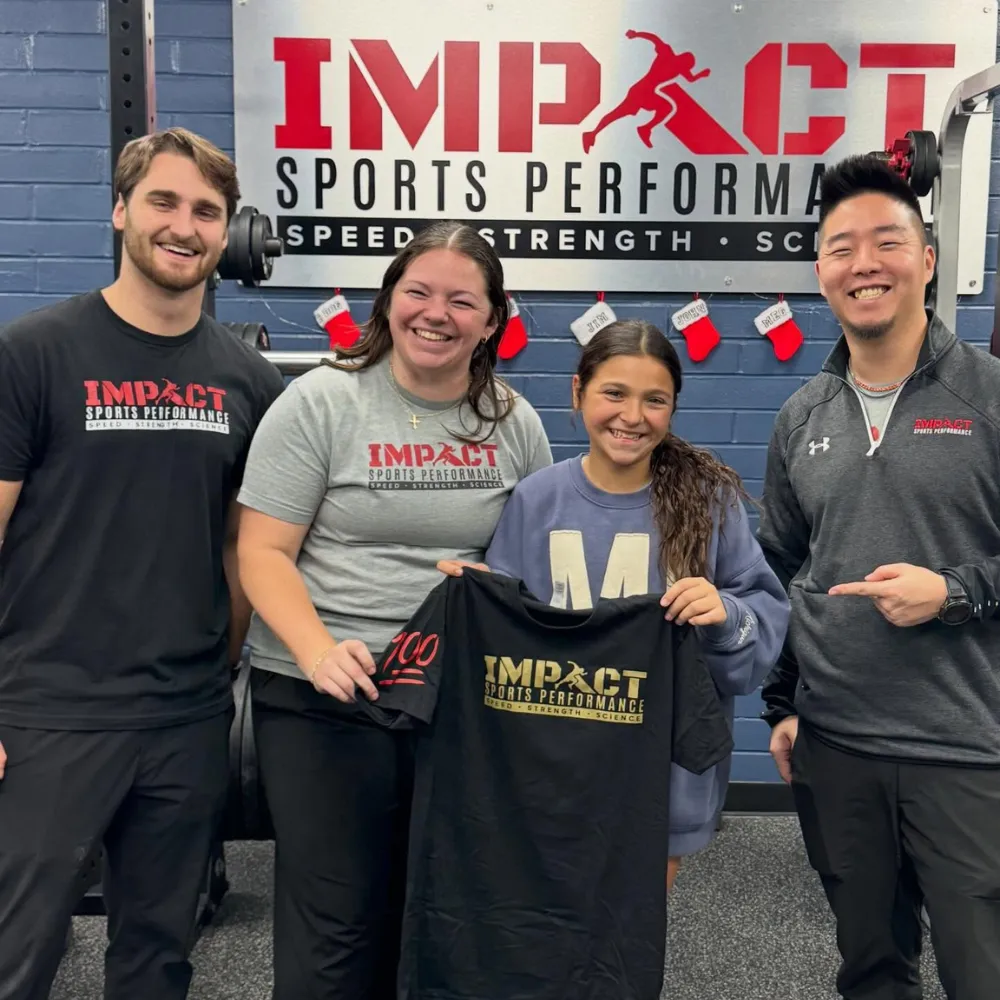 Youth athlete holding new Impact Sports Performance shirt with coach after starting training program