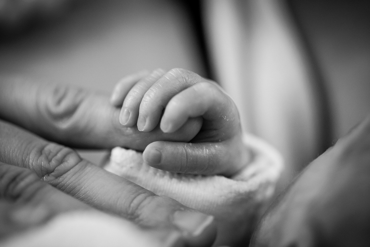 Newborn baby holding an adult's finger