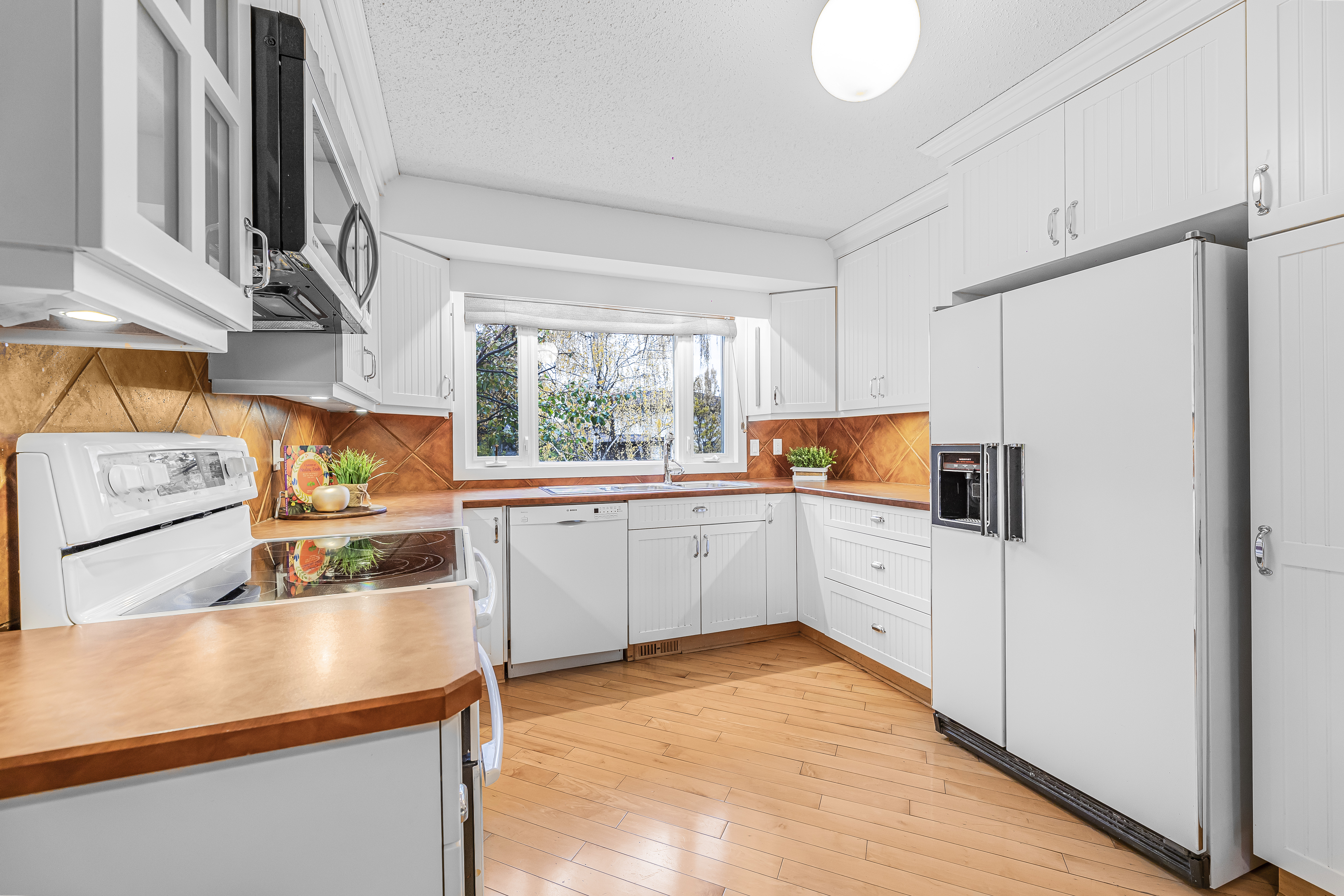 Bright staged kitchen with white cabinets, wood countertops and flooring, and a large window above the sink bringing in natural light.