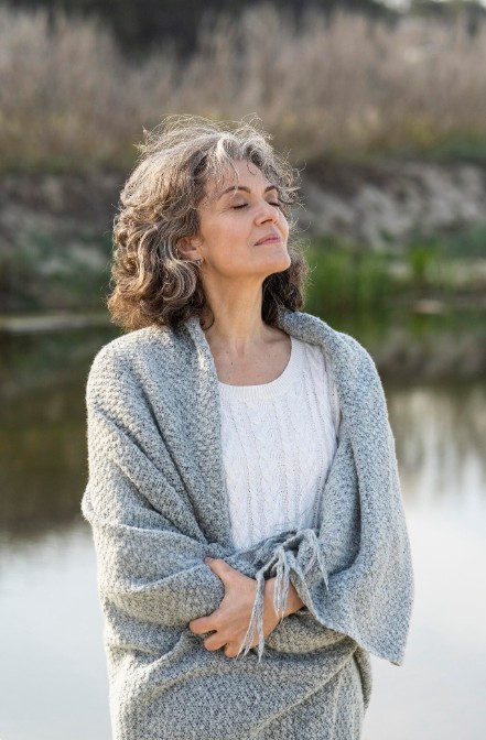 serene woman wrapped in a blanket by water, finding comfort through an acupuncture clinic in woodbury mn.