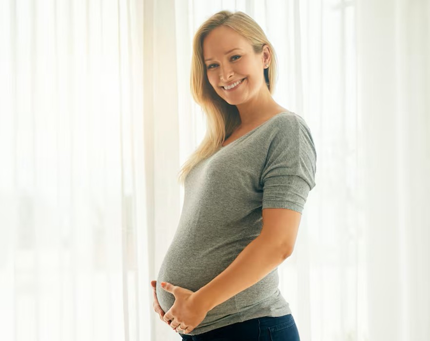 smiling beautiful woman holding her pregnant belly after successful fertility acupuncture clinic support in woodbury mn.