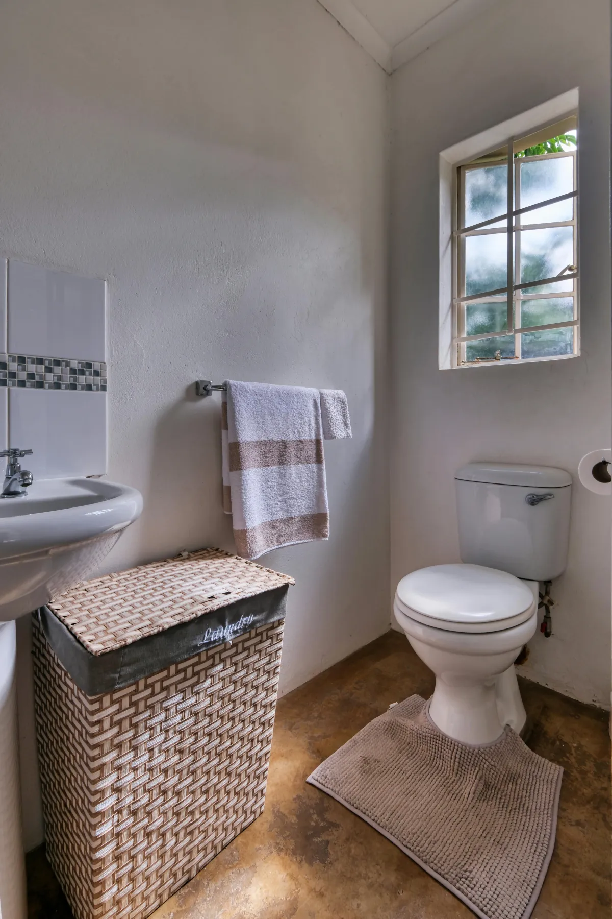 Bathroom with a toilet, towel basket, and window. 