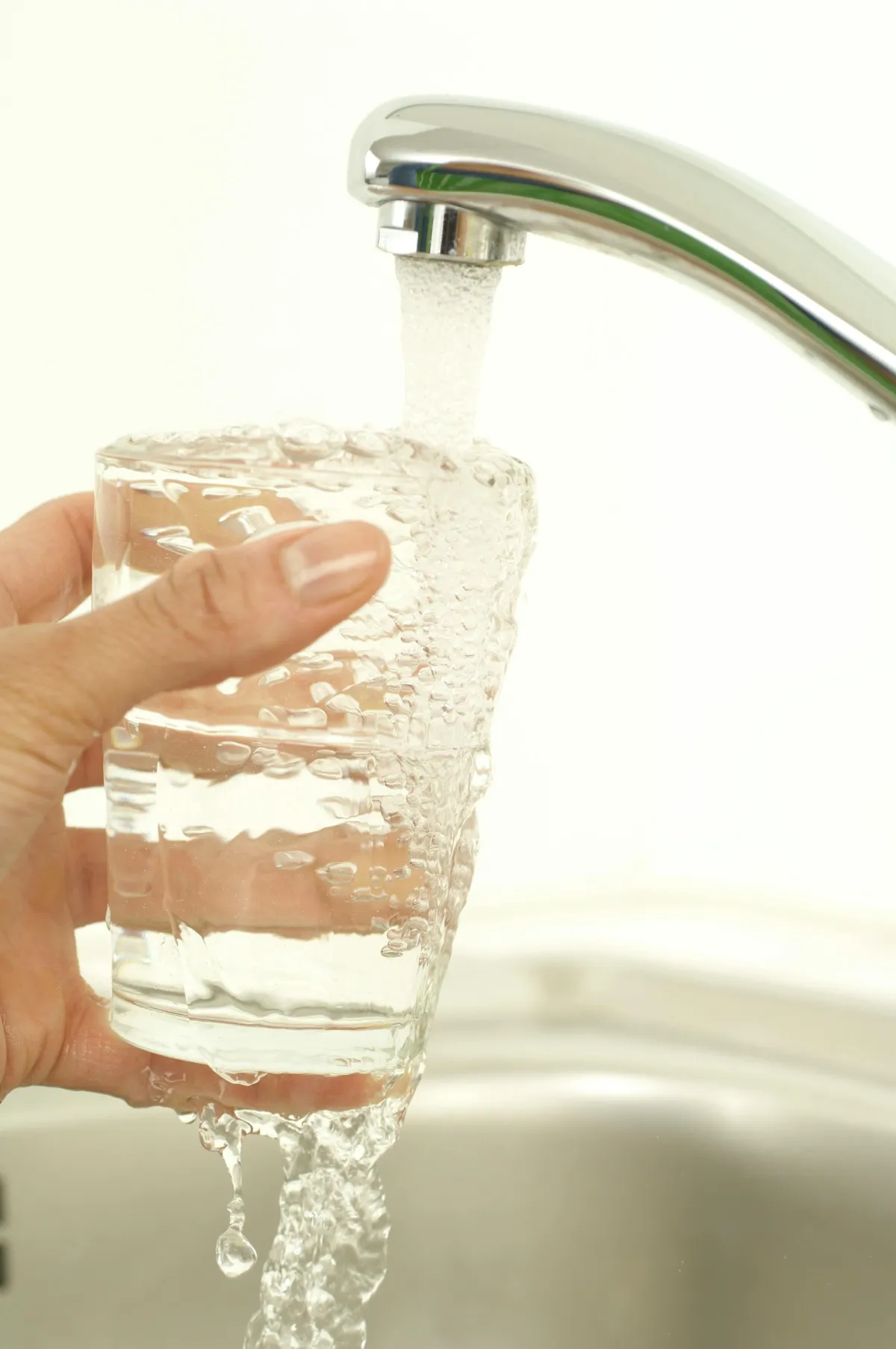 Glass of water being filled by the faucet.