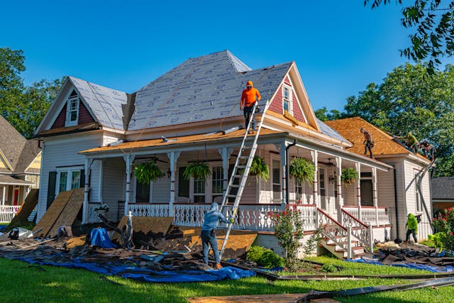 Workers repairing a tiled roof with scaffolding and corrugated metal.
