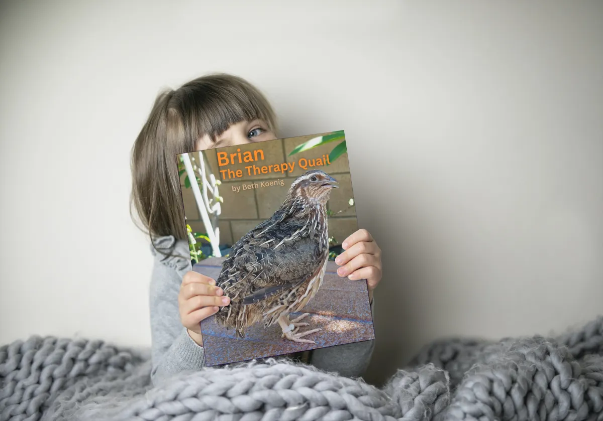 A child holds a copy of the book Brian the Therapy Quail 