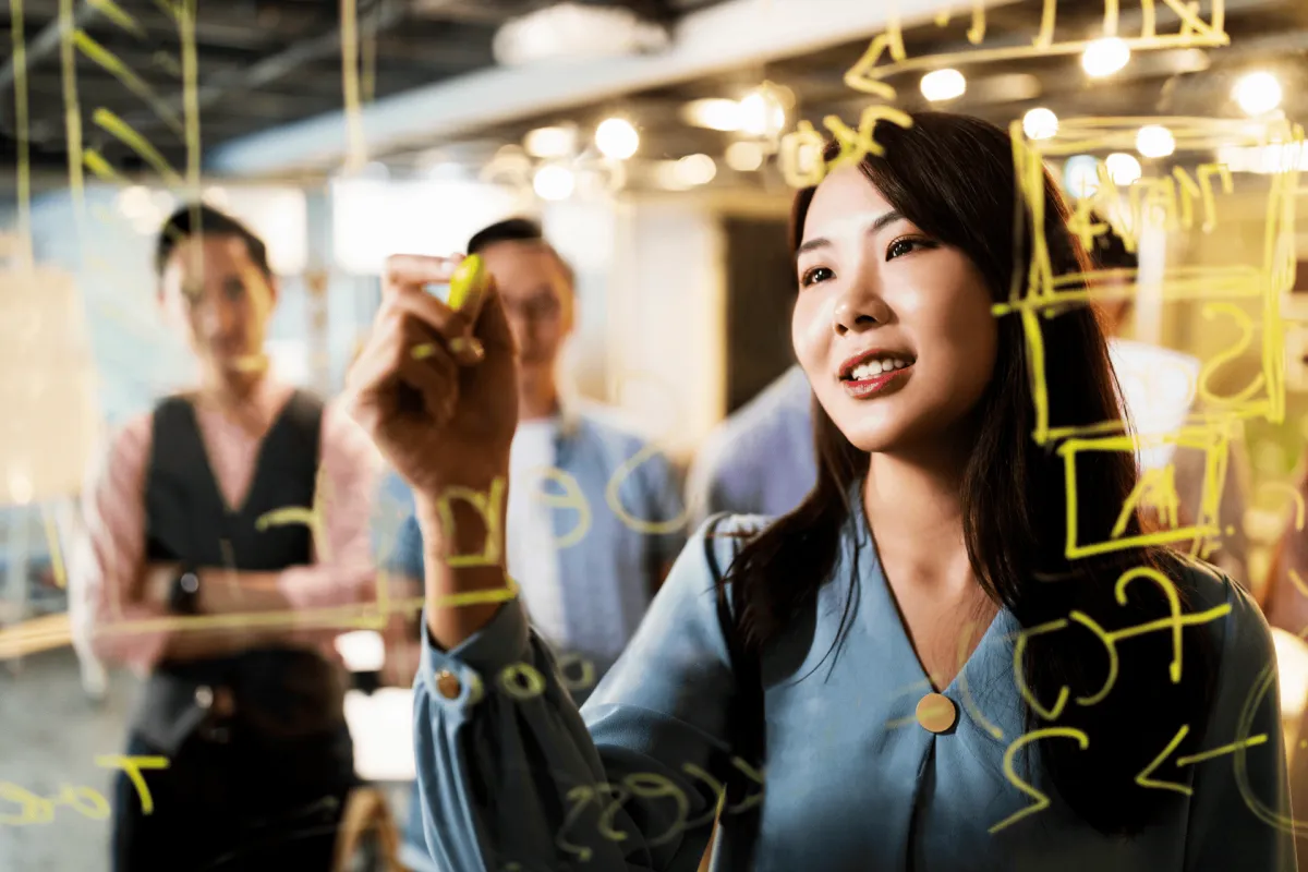 Woman writing ideas on a glass board during a team brainstorming session