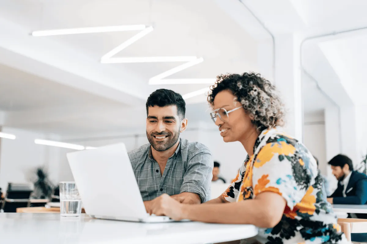 Collaborative coworkers smiling while working on a laptop in a bright office