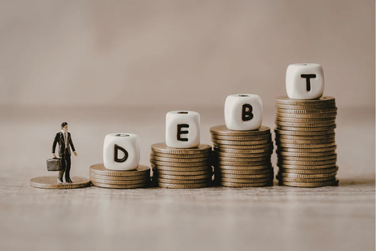 Mini figure beside stacked coins spelling DEBT