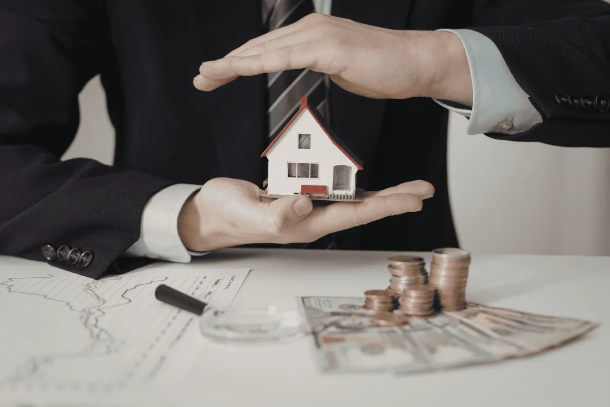 Businessperson holding model house above cash and coins