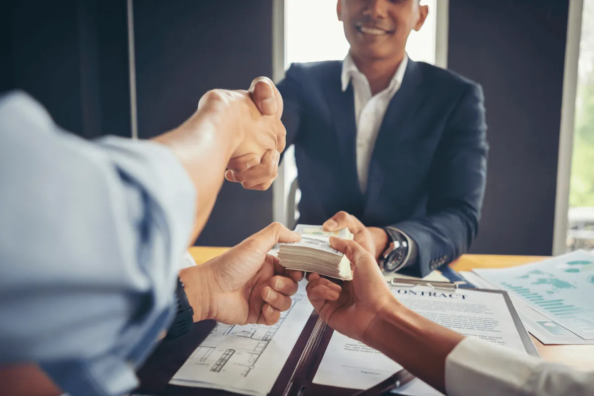 Business handshake during a cash payment over contract documents