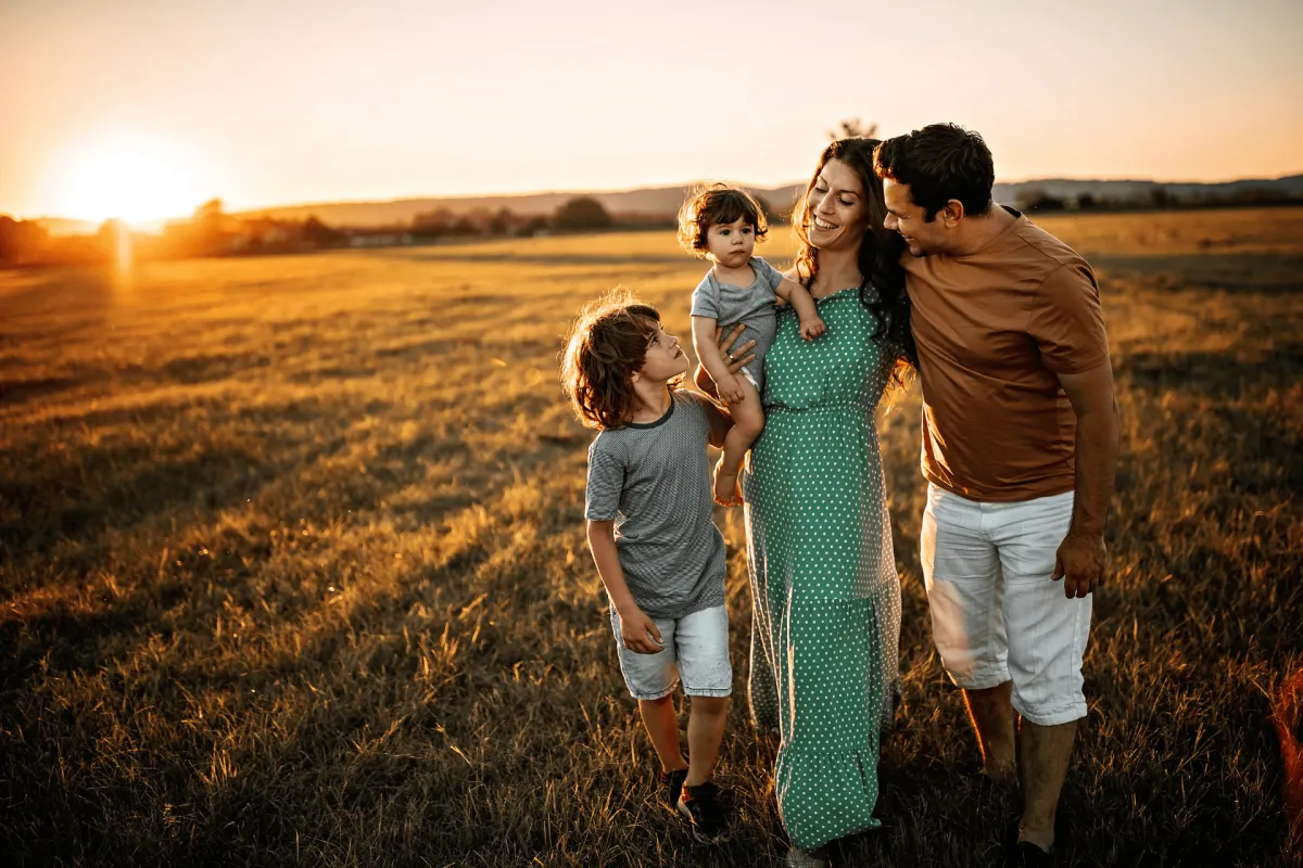 Family of four walking together through a field at sunset